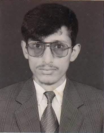 Young man in a suit and tie with glasses, black and white portrait.
